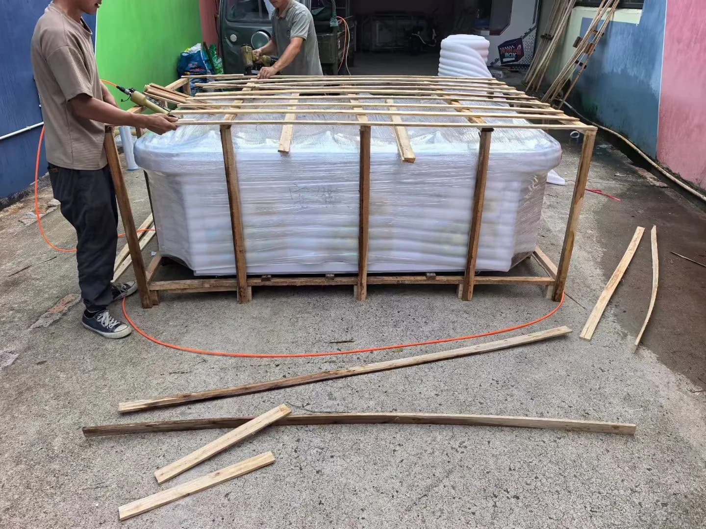 Jisun packing workers securing a wooden export frame around a foam-wrapped amusement machine
