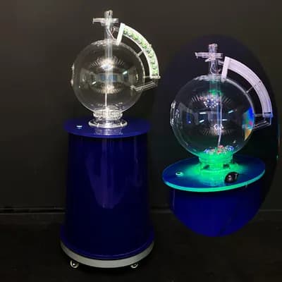 Side-by-side views of the lottery machine, one unlit on its blue stand and one glowing green with numbered balls inside