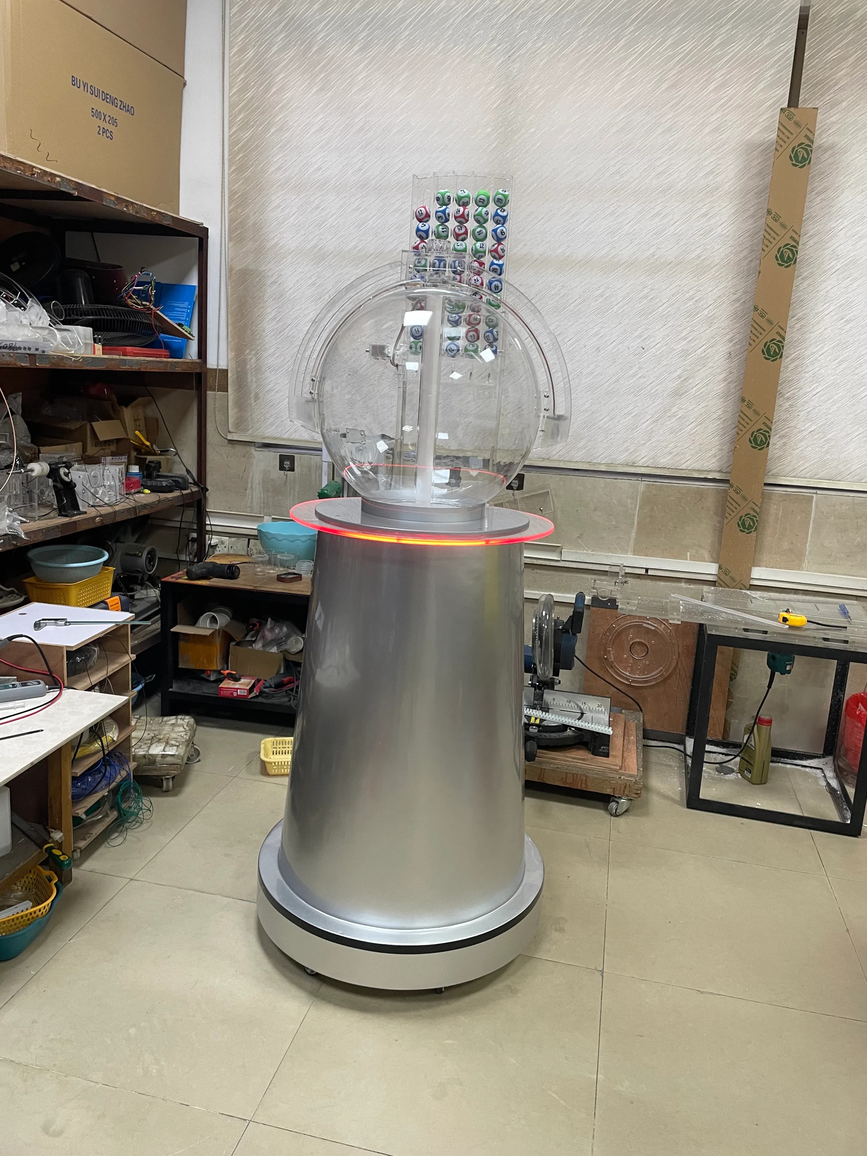 Clear top-ball lottery chamber mounted on a tapered silver column with red LED ring
