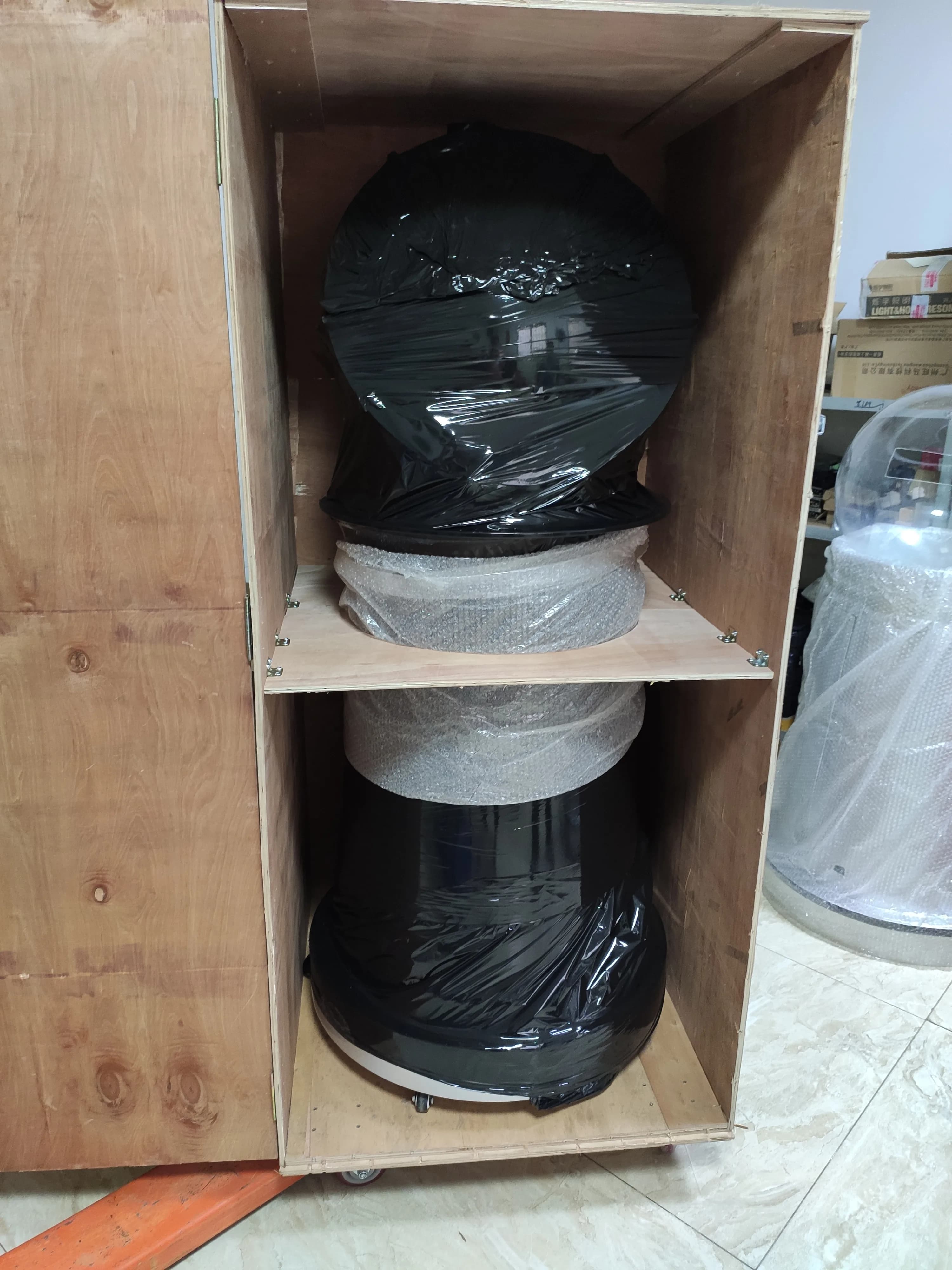 Film-wrapped round lottery machine secured in a divided wooden export crate