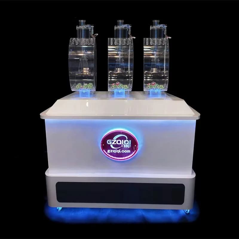 Front view of a three-cylinder lottery ball machine with clear acrylic drums and a glowing round logo on the white base.