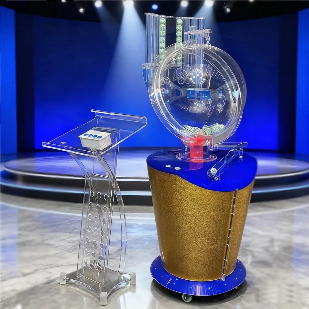 Gold air blower lottery machine with clear acrylic console podium on a blue-lit studio stage, numbered balls loaded.