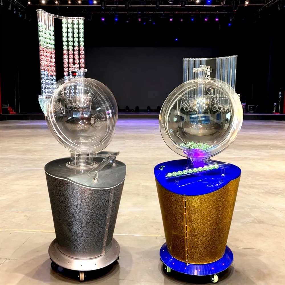Two YP600 air-blown bingo ball machines with clear spherical chambers and numbered ball racks standing on an event stage